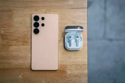 Peach smartphone and wireless earbuds on wooden table