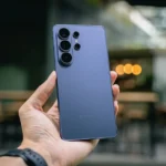 Hand holding a blue smartphone with multiple cameras.