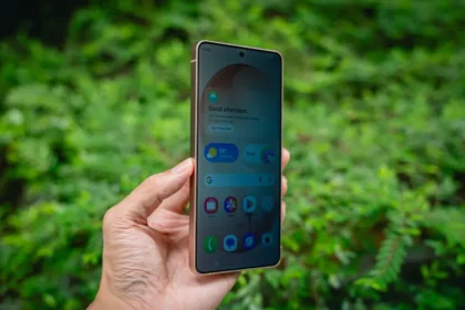 Hand holding a smartphone with green foliage background.