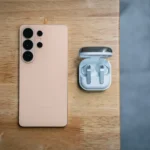 Peach smartphone and wireless earbuds on wooden table