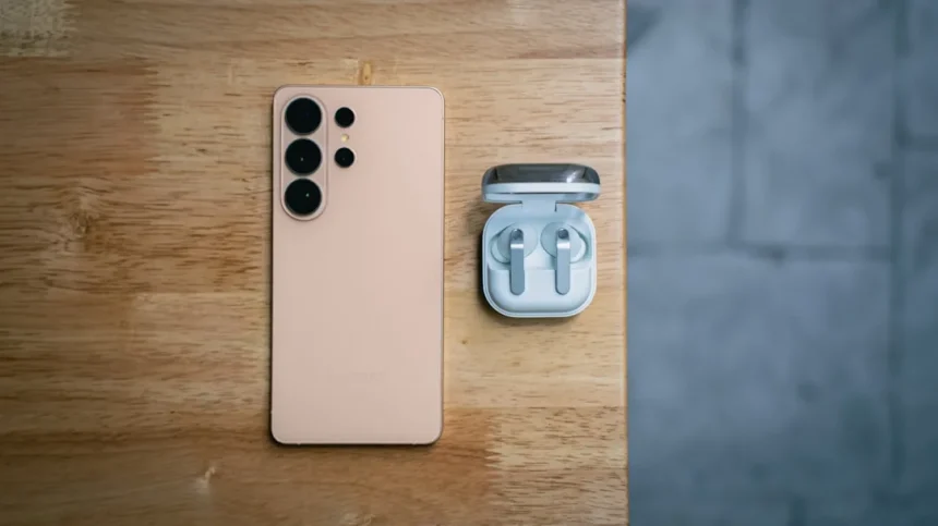 Peach smartphone and wireless earbuds on wooden table