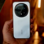 Hand holding a silver smartphone with a large camera lens.