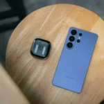 A blue smartphone and earbuds on a wooden table