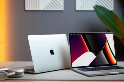 two apple laptops sitting on a table next to a plant